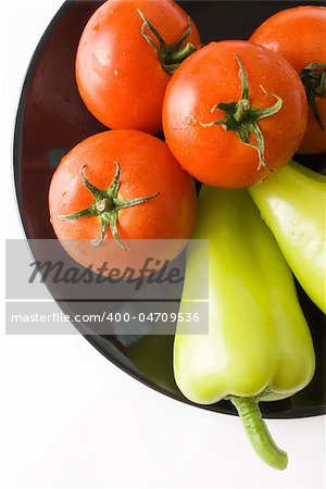 Tomatoes and peppers washed and placed in a black ceramic plate isolated on white background top view