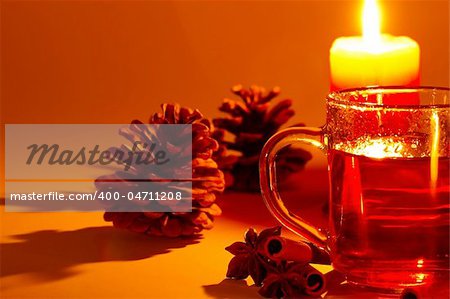 red tea in a glass, cinnamon sticks, star anise and a conifer cone at candle light