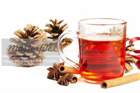 red tea in a glass, cinnamon sticks, star anise and some conifer cones on white background