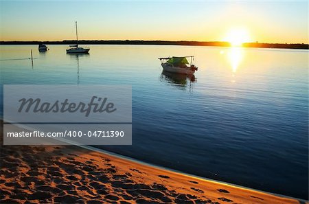 Sun streams over small boats in a still lagoon at dawn.