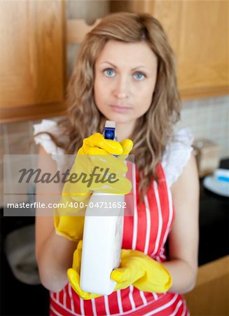 Beautiful blond woman holding cleansing agent into the camera in the kitchen