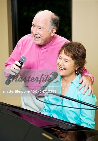 Senior couple performs.  They both sing while she plays piano.