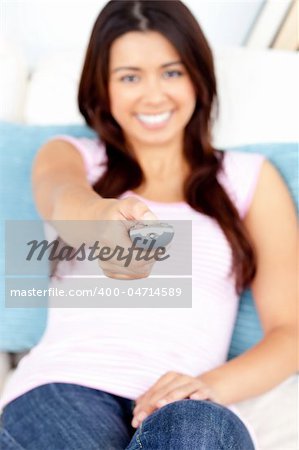 Captivating asian woman holding a remote smiling at the camera sitting in the living room