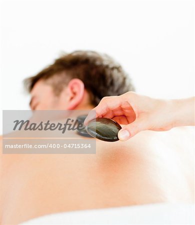 Close-up of a positive young man having a back massage with hot stone in a spa center