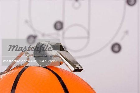 A silver whistle laying on an orange basketball in front of a diagram of the game plan.