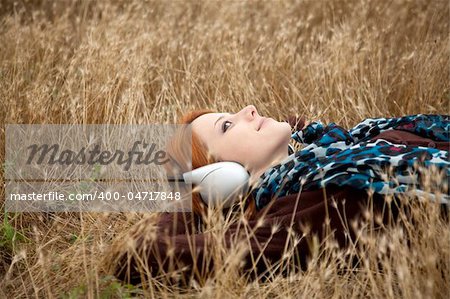 Young  smiling fashion with headphones lying at field.