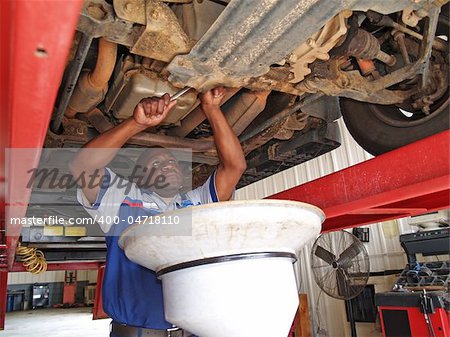 Auto mechanic performing an oil change with the car on a lift in a service station garage.