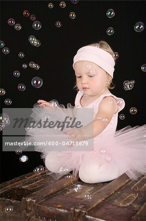 Cute blond toddler in ballet tutu reaching out to touch bubbles