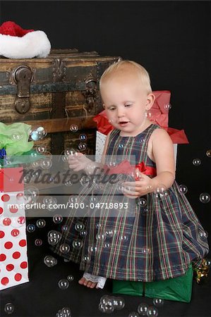Cute blond toddler infront of an antique trunk with christmas presents