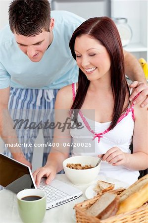 Bright couple using a laptop while breakfast at home in the kitchen