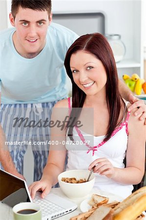 Smiling couple using a laptop while breakfast at home in the kitchen