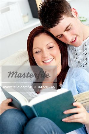 Happy couple reading a book in the living-room lying on the sofa