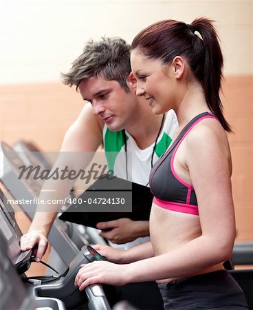 Beautiful athletic woman standing on a running machine with her personal coach in a fitness center