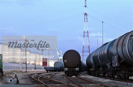 Oil tank cars standing on rail tracks in industrial area; twilight scene