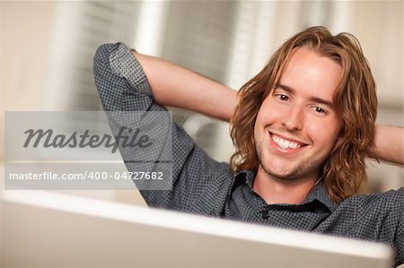 Happy Young Man Using A Laptop Computer with Hands Behind His Head.