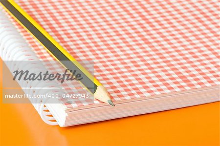 pencil and notebook over an orange background