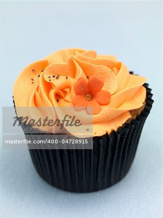 A freshly baked cup cake with orange frosting