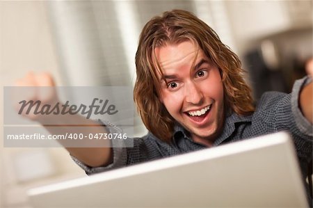 Happy, Cheering Young Man Using A Laptop Computer and Cheering with Fists in the Air.