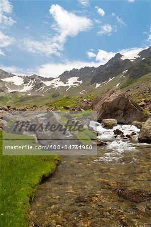 A stream with green grass banks of the mountains in the background.