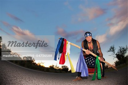 Indigenous man squatting in the middle of a road with ceremonial pole and flags in the middle of a road with ceremonial pole representing seven directions