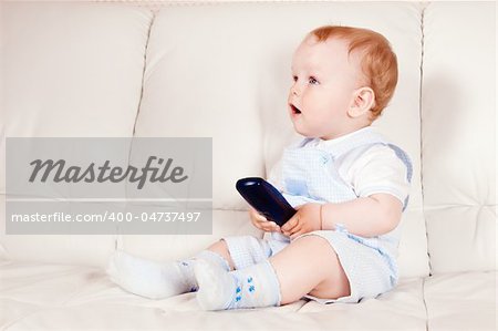 The baby sits on a white sofa with the TV panel