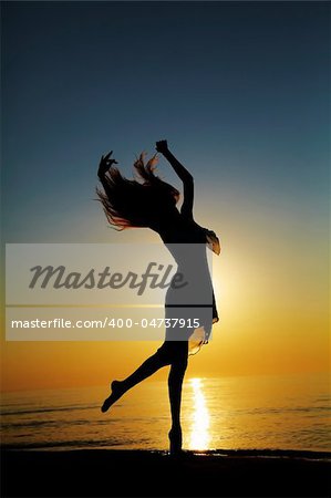 Girl dances on the beach at sunset. Natural light and dark. Artistic colors added. Vertical photo