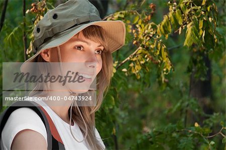 beautiful young woman standing  in forest with backpack, smiling and looking away from camera