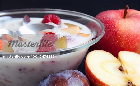 Glass bowl filled with yogurt mixed with fruit pieces arranged with spoon and some fruits around