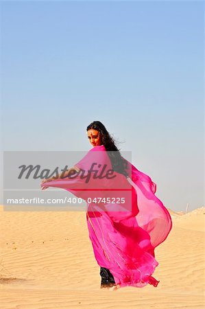 Beautiful young woman  in pink eastern dress dancing in arabic desert