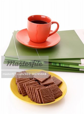 Chocolate cookie and cup of coffee on magazines isolated on white
