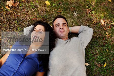 A couple laying on grass in a park daydreaming.  Focus on the womans eyes