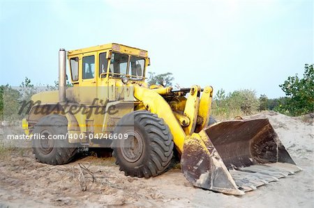 Old wheel loader bulldozer with bucket standing in sandpit outdoors