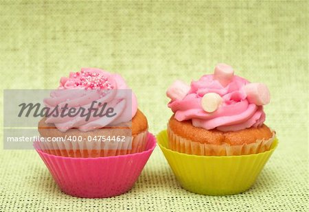 Fresh vanilla cupcakes in pink cup with strawberry icing on decorative background