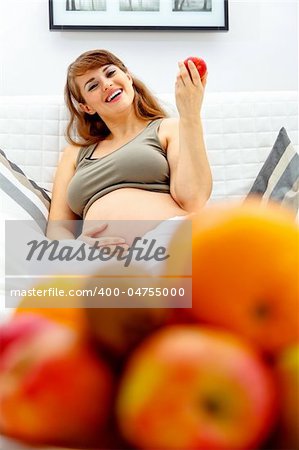 Smiling  beautiful pregnant woman relaxing on couch at home and  holding fruit in hand