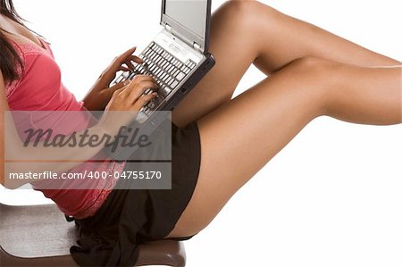 Perfectly shaped legs, hips, and torso of unrecognizable female student sitting on the desk with notebook portable PC on her lap. She is typing on this computer keyboard