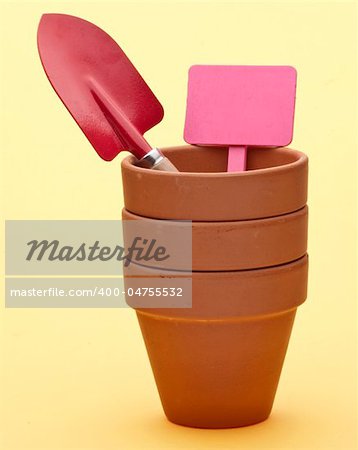 Stack of Garden Pots with Shovel and Blank Garden Sign on a Yellow Background.