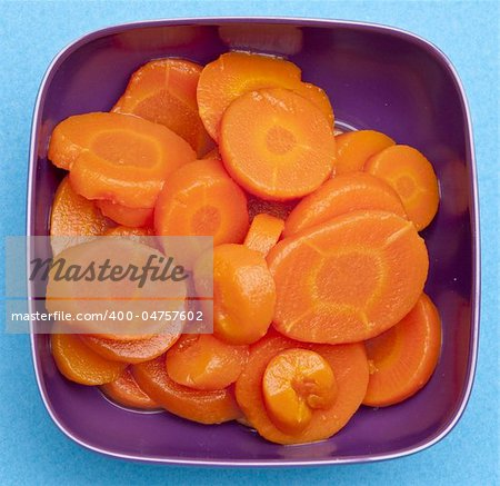 Bowl of canned carrots on a vibrant blue background.