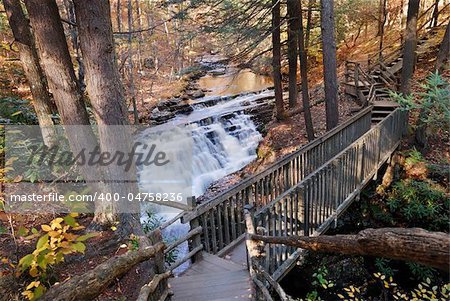 Autumn creek with hiking trail and rocks in woods with colorful foliage.