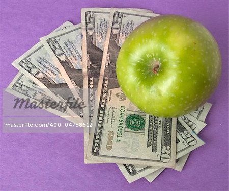 A green apple sits on top of a pile of $20 bills to illustrate the cost of education, food, or health care.