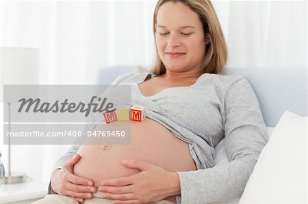 Relaxed woman looking at mom letters on her belly and resting on a bed
