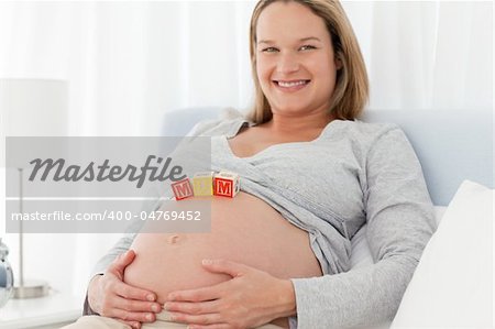 Portrait of a future mom with baby letters on her belly and smiling at the camera