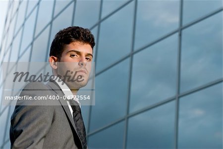 Young businessman looking to camera on modern building background