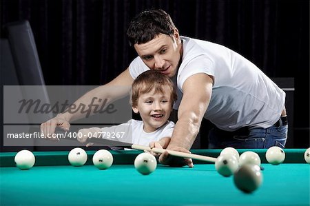 The young man learns the little boy to play billiards