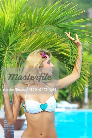 Beautiful woman near swimming pool under palm tree