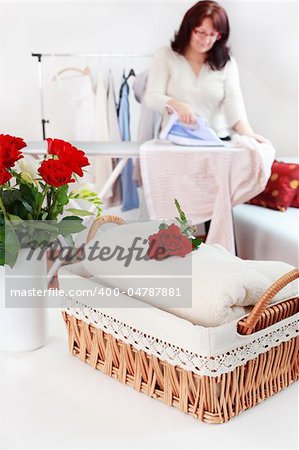 Basket with laundry and ironing board with housewife in background