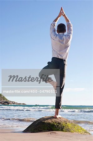 Businessman doing equilibration exercise on a rock at the beach