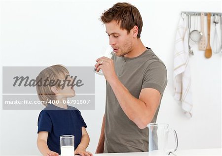 Happy dad and son drinking milk together in the kitchen