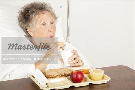 Senior woman in the hospital, eating lunch and drinking from a straw.