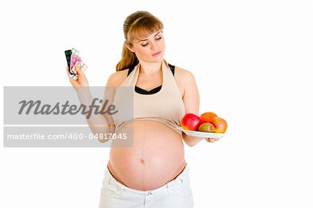 Pensive pregnant woman making choice between pills and fruits isolated on white