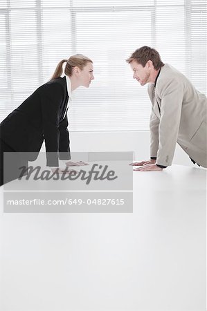 Rival business people leaning over desk